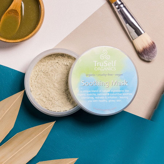 Soothing face mask jar with open lid showing pale powder; makeup brush and jar