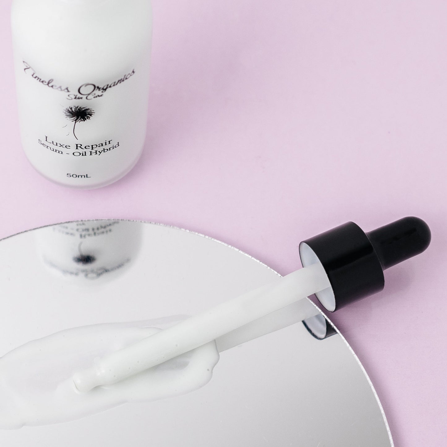 Dropper releasing white serum from luxe repair serum-oil hybrid bottle