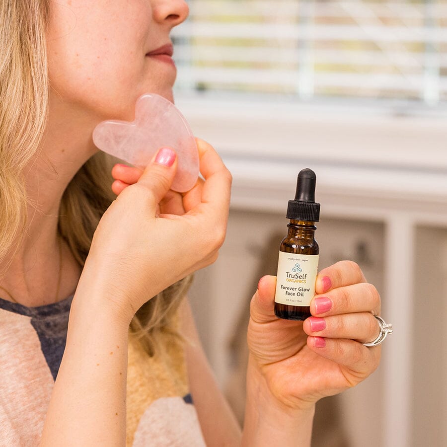 Anti-aging facial massage kit: rose quartz gua sha on cheek with face oil bottle