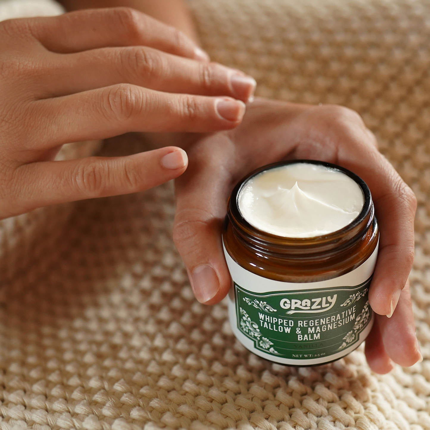 Whipped tallow & magnesium balm jar held open with white cream; vanilla label visible