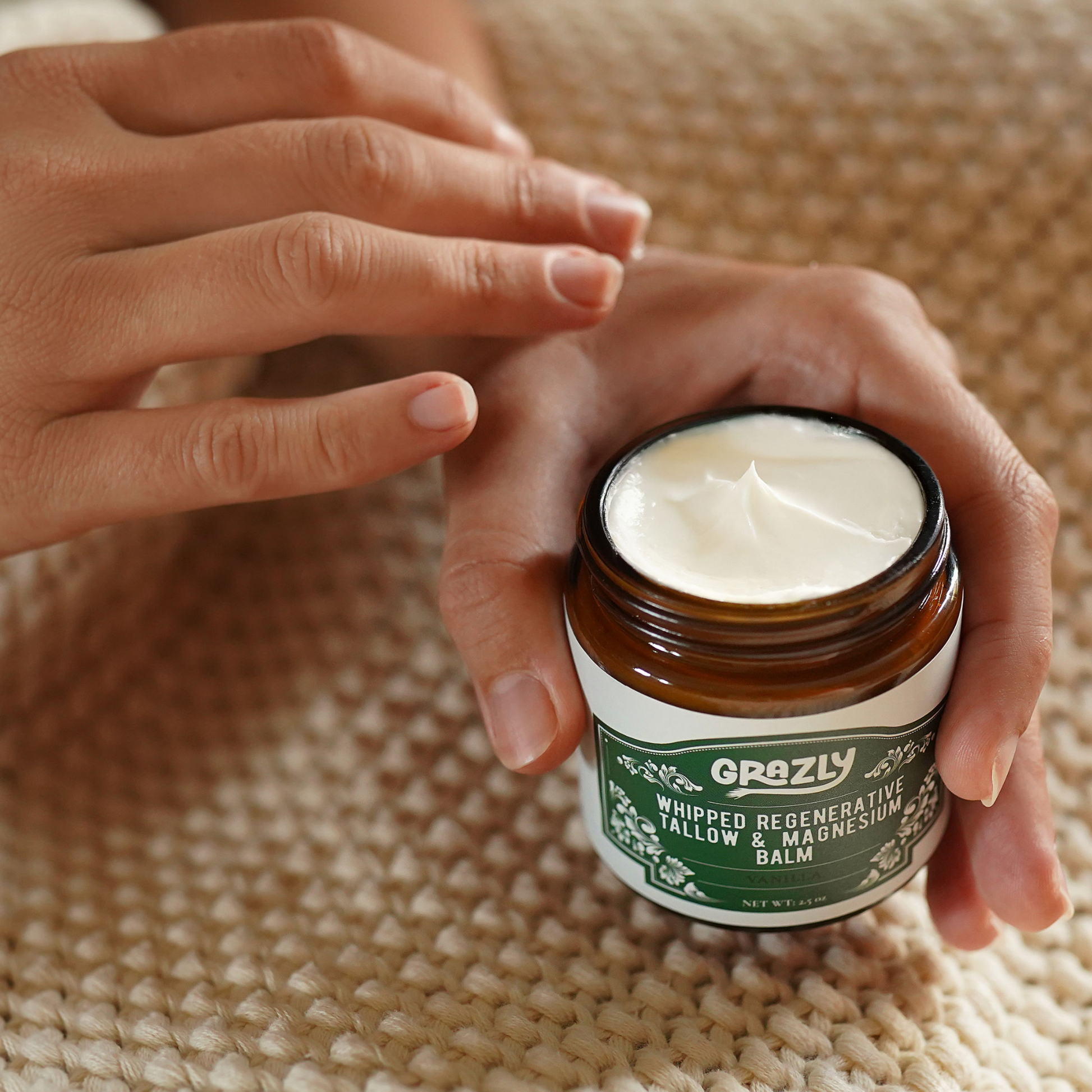 Whipped tallow & magnesium balm jar held open with white cream; vanilla label visible