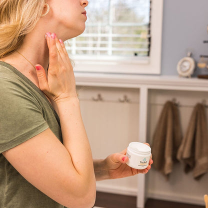 Herbal infused moisturizer jar held by person while applying to face
