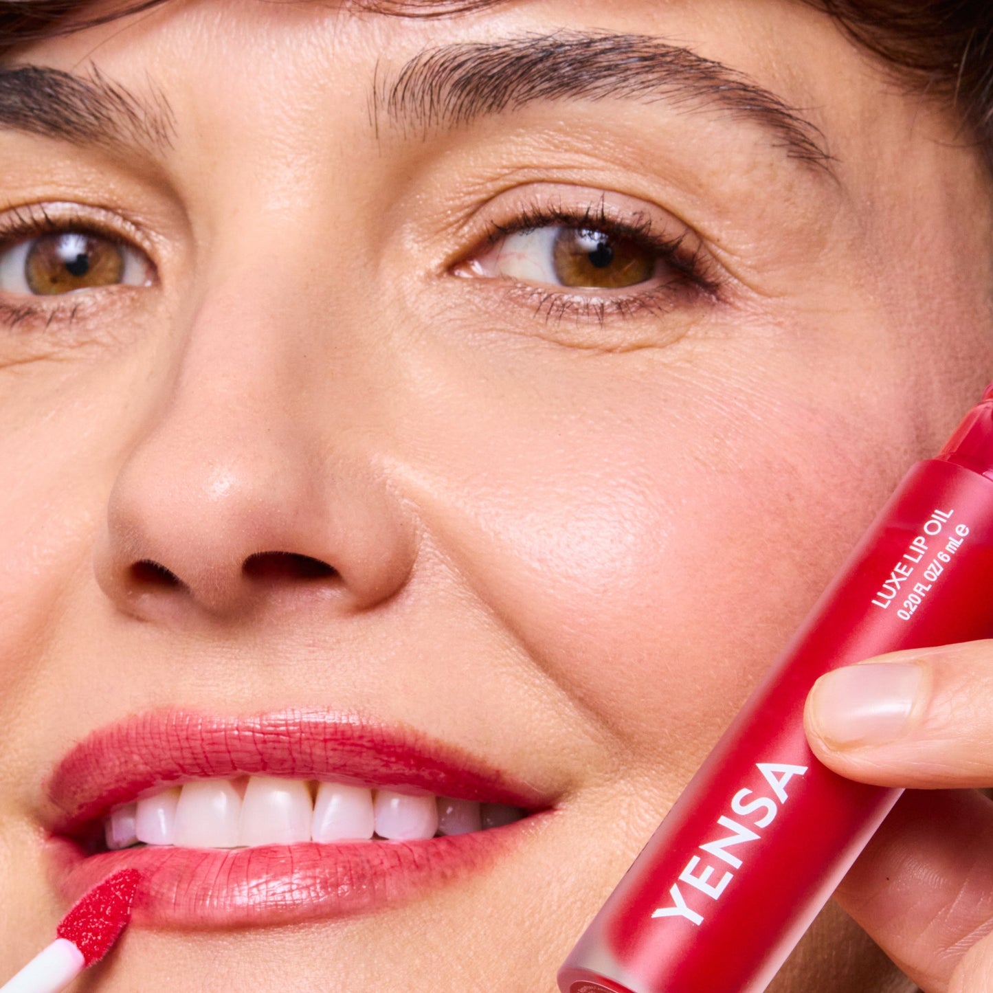 Lip oil wand applying red gloss to lips; YENSA tube held near mouth