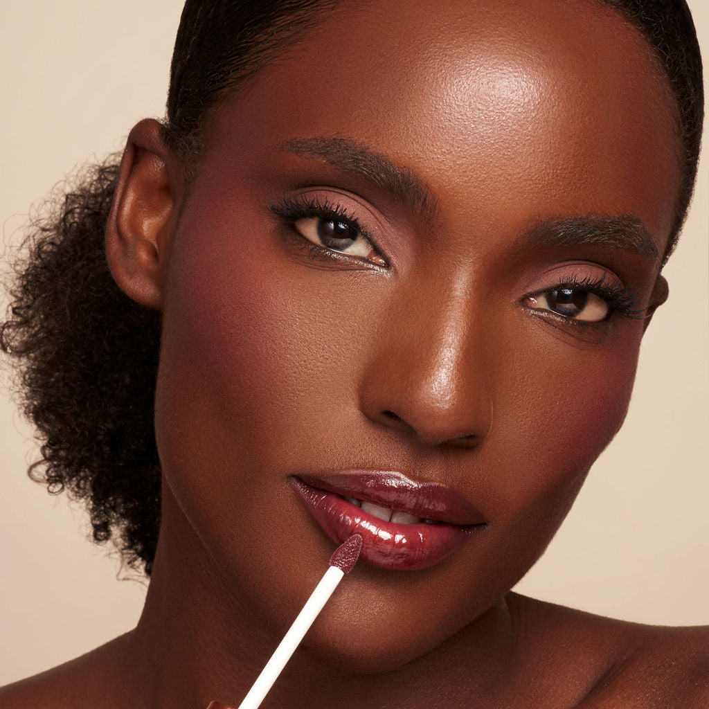 Lip oil applicator applying berry gloss to lips with shiny finish