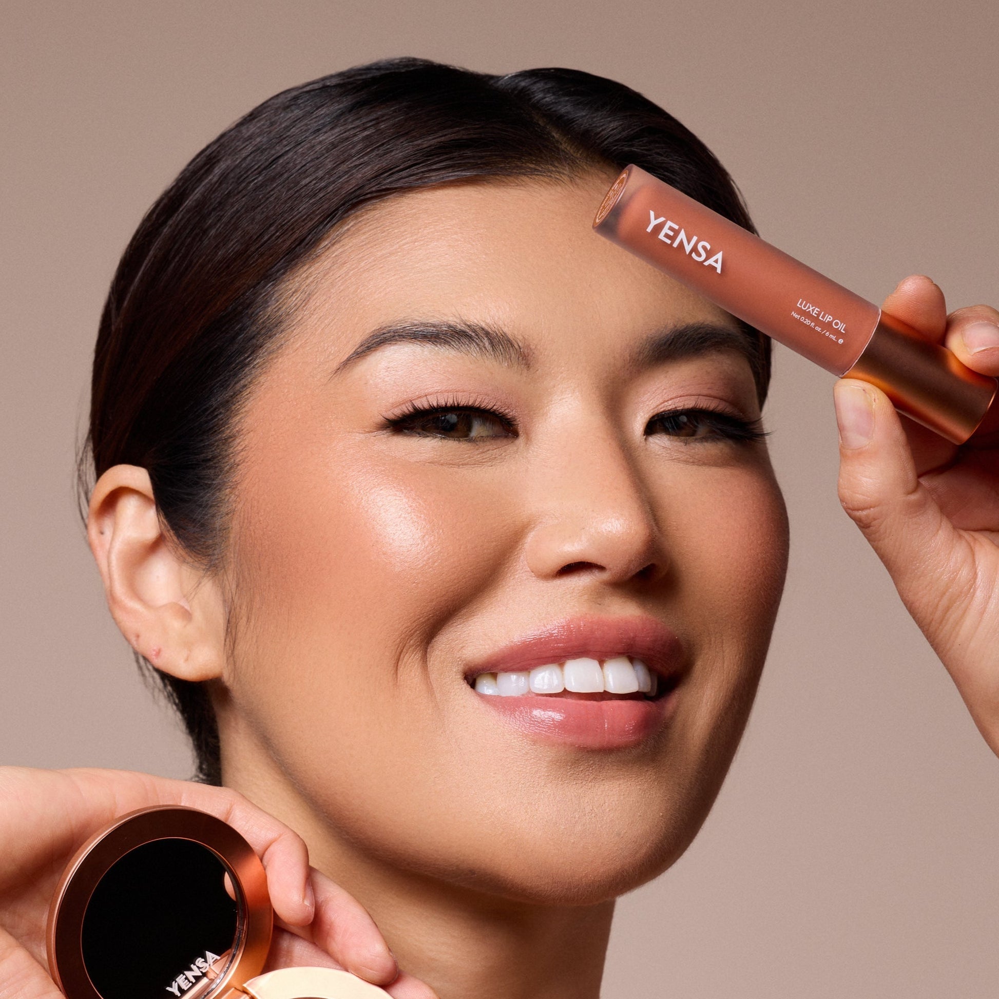 Luxe lip oil wand in rose-gold held near face with tinted lips and smile