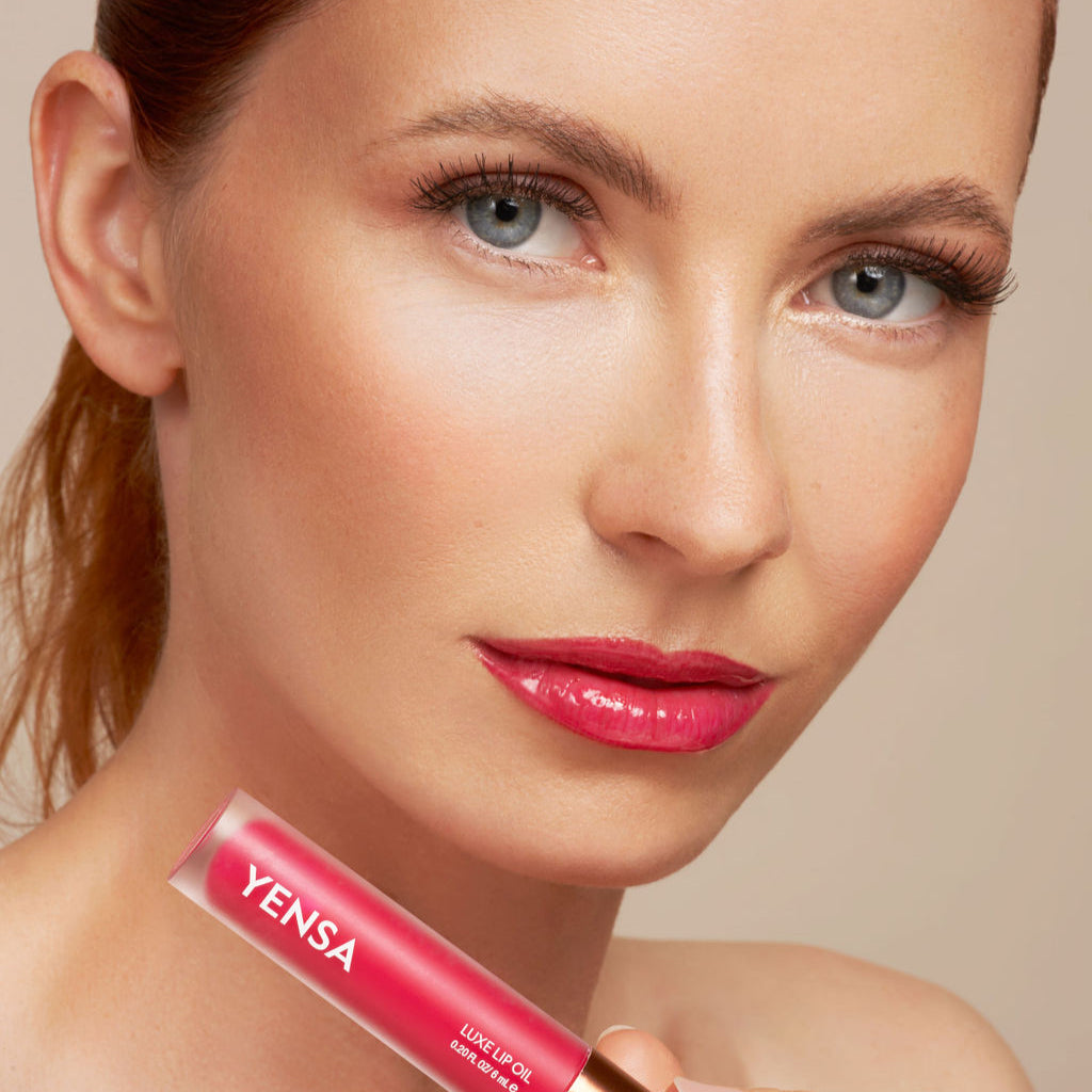 Pink lip oil tube held near glossy red lips with sparkling finish