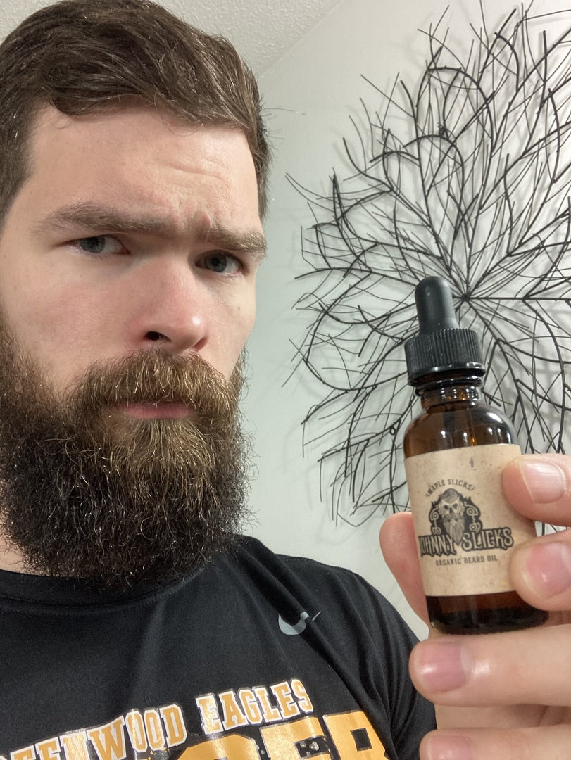 Man holding Johnny Slicks organic beard oil bottle near his beard, amber bottle with black cap
