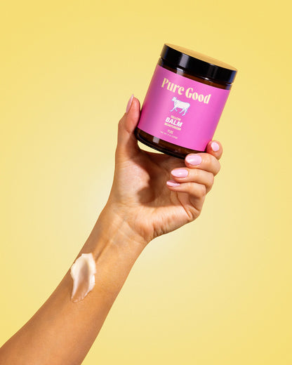 Hand holding tallow balm jar, pink label and black lid; balm smear on wrist