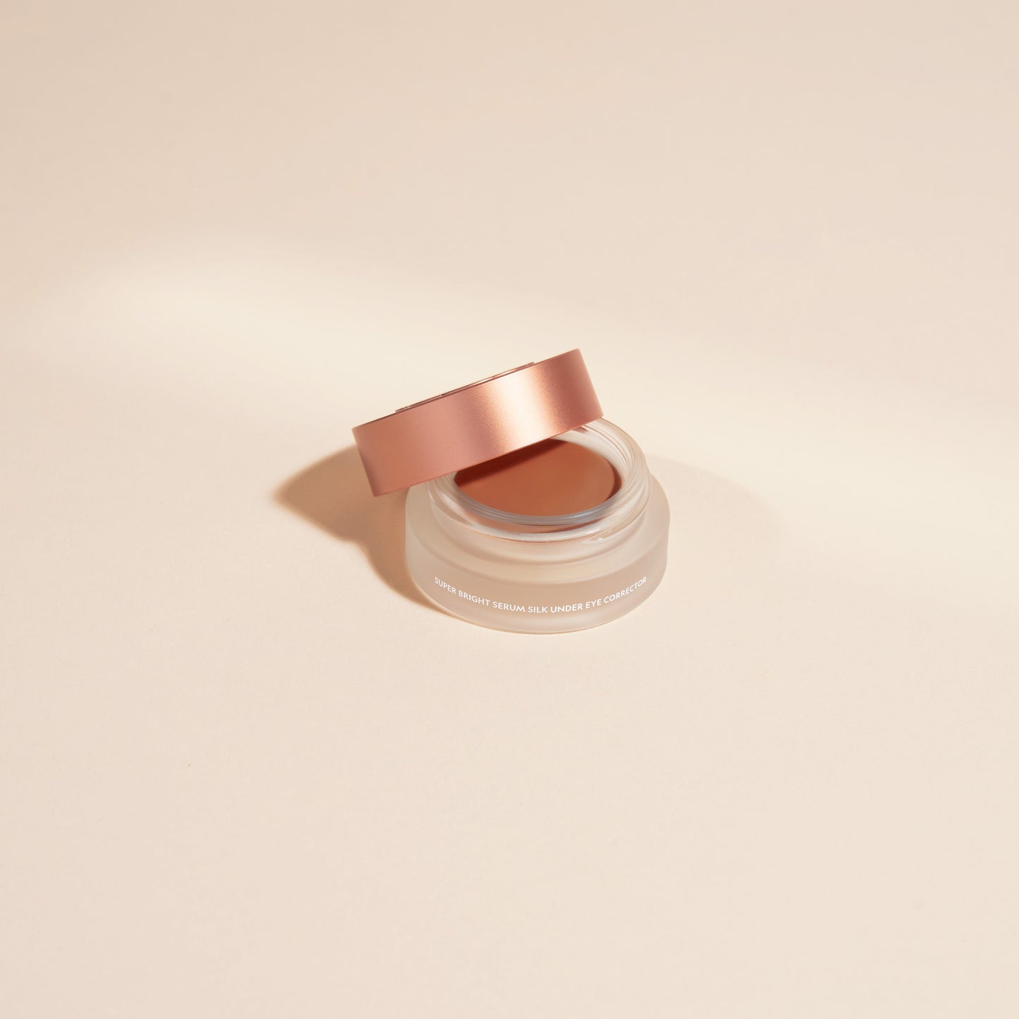 Under-eye serum in a clear jar with rose-pink lid and cream shade inside