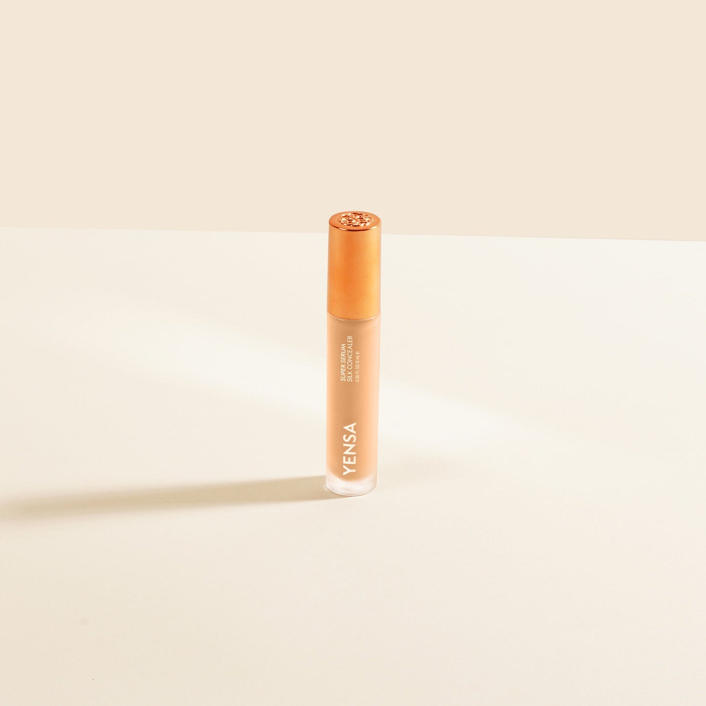 Concealer serum bottle with bronze cap and light beige liquid, upright view