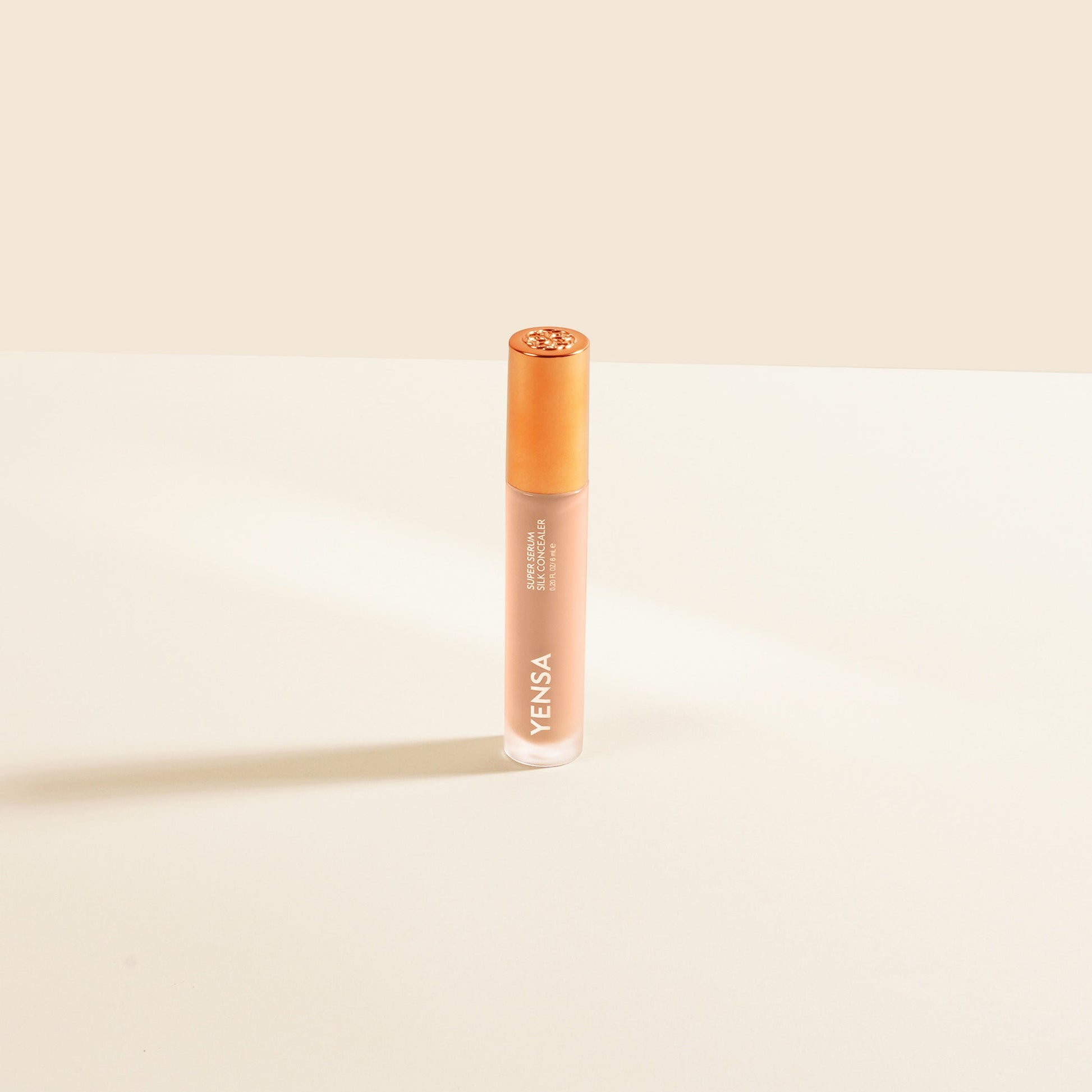 Concealer serum bottle with bronze cap and light beige liquid, centered view