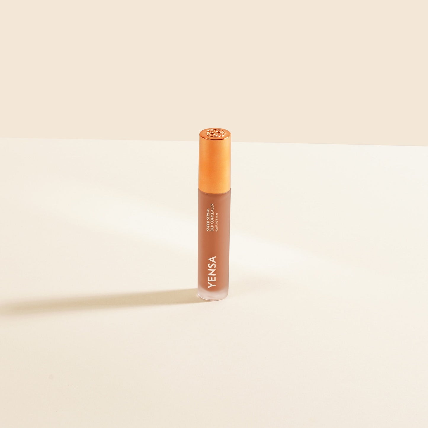 Concealer tube standing upright, light peach liquid with rose-gold cap