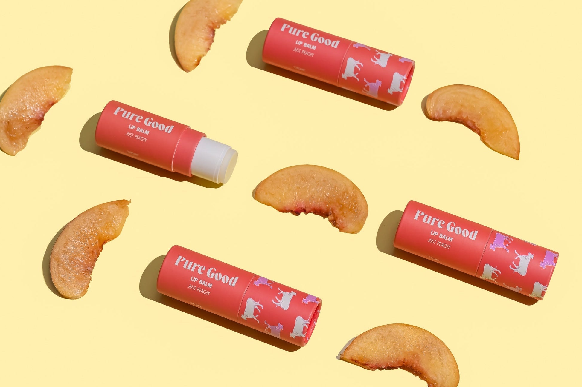 Tallow lip balm tubes with peaches around them, including one peach-colored Just Peachy tube