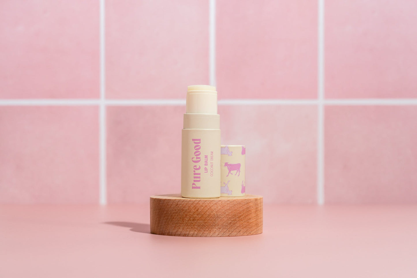 Tallow lip balm tube with pastel purple Pure Good label and cream cap on wooden base
