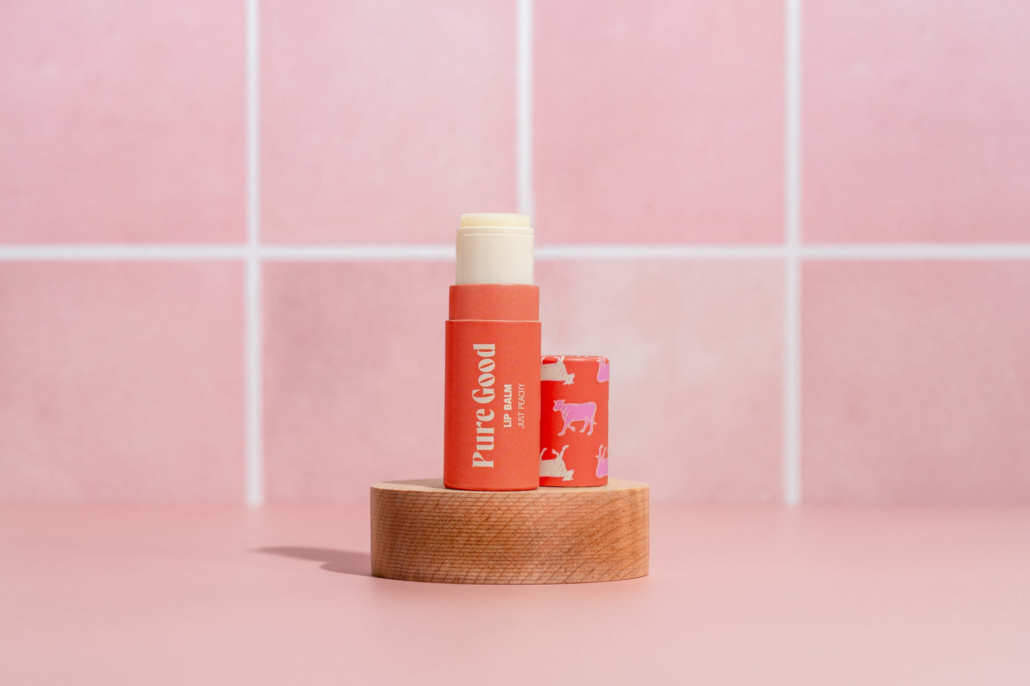 Tallow lip balm tube with red-orange Pure Good label and cream cap on wooden base