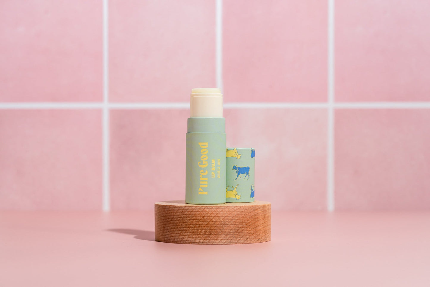 Tallow lip balm tube with light green Pure Good label and cream cap on wooden base