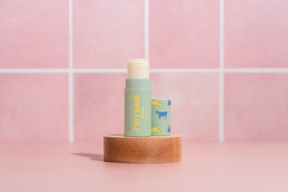 Tallow lip balm tube with light green Pure Good label and cream cap on wooden base