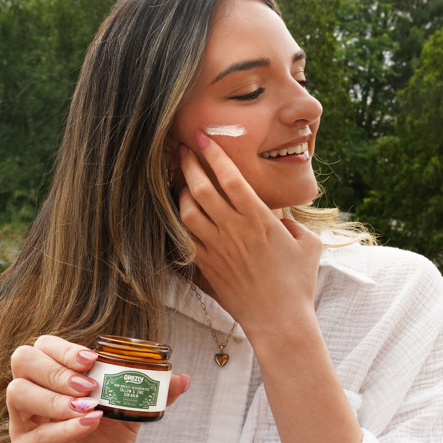 Sun balm jar in hand as balm is applied to cheek, unscented label