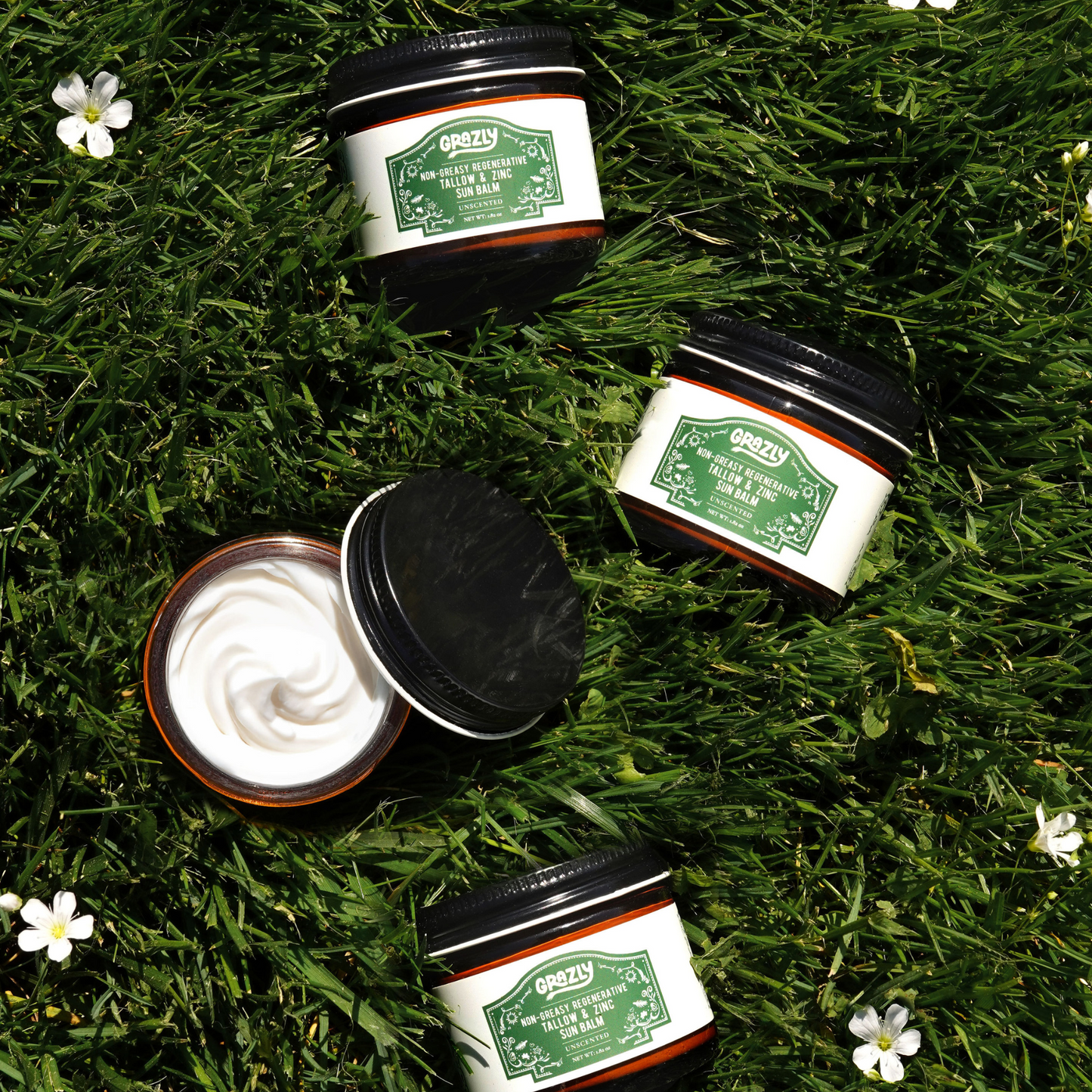 Sun balm jars on grass, one lid open showing creamy balm