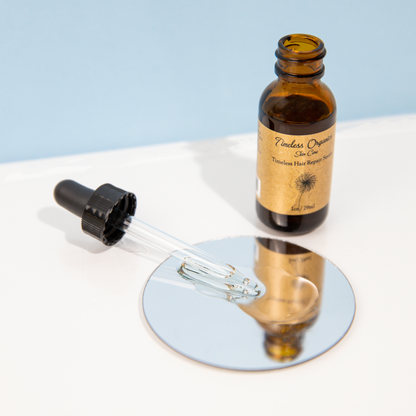 Hair repair serum bottle with dropper releasing clear liquid on glass plate