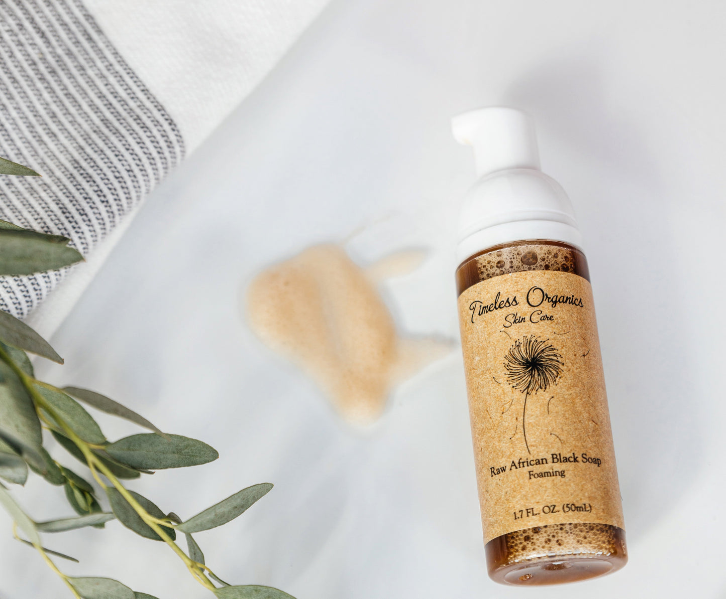 Raw African Black Soap foaming cleanser bottle with white foamy lather beside it.