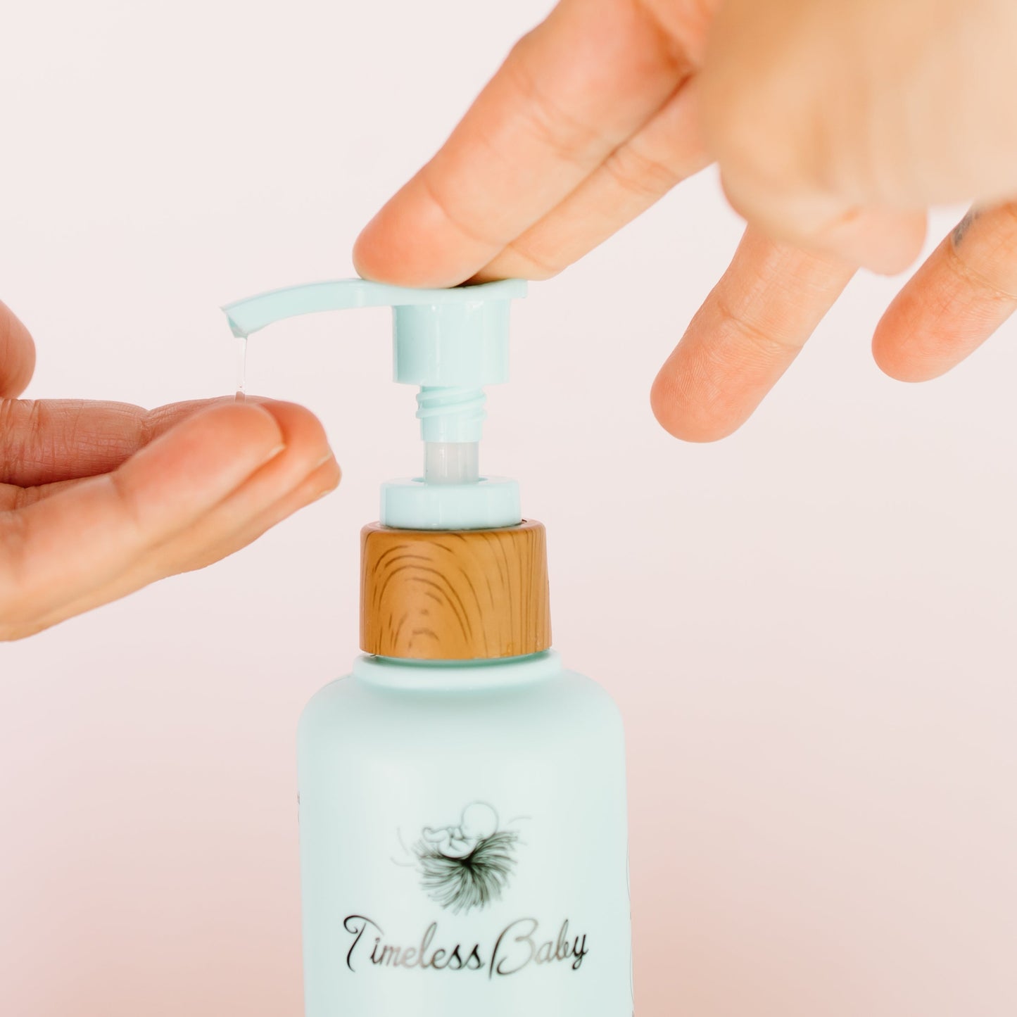 Hands pressing the wooden pump on a light blue baby hair & body wash bottle
