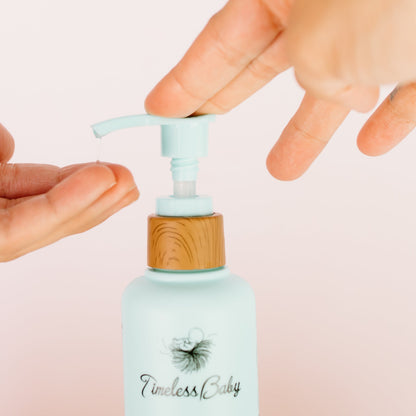 Hands pressing the wooden pump on a light blue baby hair & body wash bottle