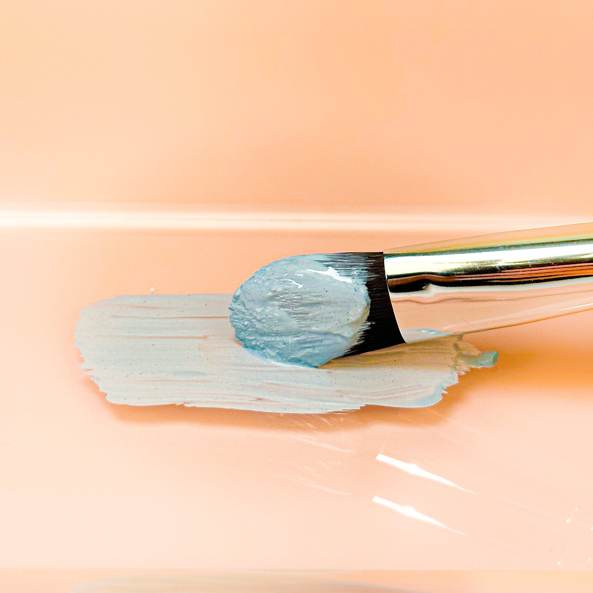 Blue clay face mask paste spread on skin with flat brush