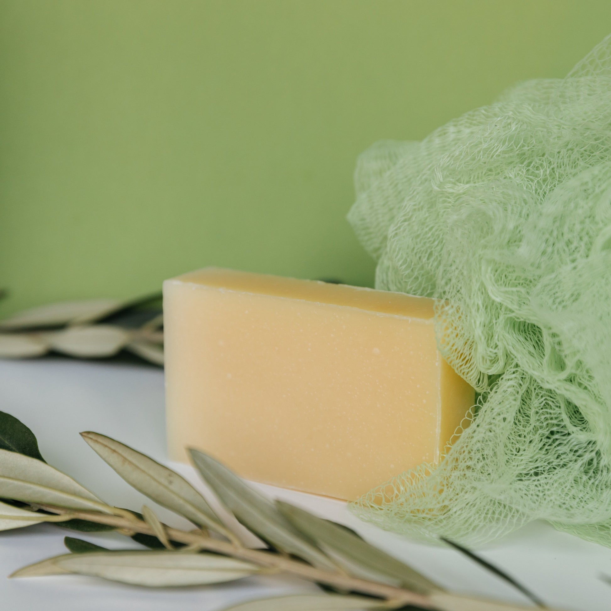 Cream shaving soap bar with loofah and herb sprigs beside it